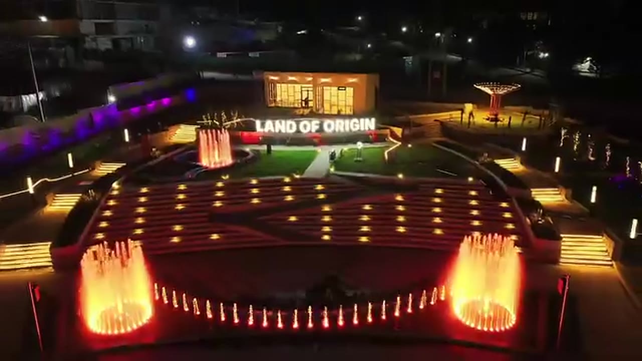 A square lit with lights and the words Land of Origin at night